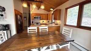Una mesa de comedor de madera con sillas, una cocina con armarios de madera, una estufa y un refrigerador.