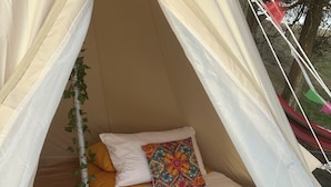 A cozy tent-style room with two beds, white bedding, a colorful pillow, and a small plant.
