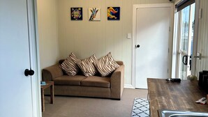 A room with a wooden floor, a brown sofa with striped pillows, a small table, and a kitchen area with a sink and countertop.