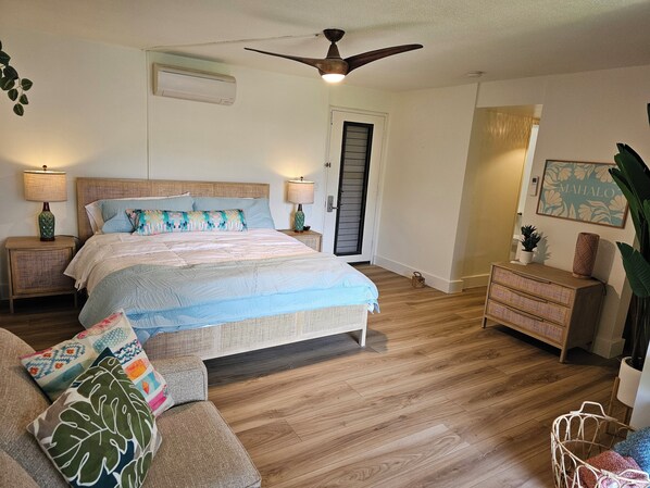 A bedroom with a bed, bedside tables, a ceiling fan, a door, and a dresser. - Gorgeous Remodeled hotel suite in Princeville w/ pools & beach access, sleeps 4 (Princeville)