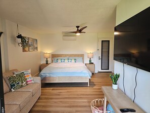 A bedroom with a bed, two bedside tables with lamps, a ceiling fan, a TV, a sofa, and a potted plant. - Gorgeous Remodeled hotel suite in Princeville w/ pools & beach access, sleeps 4 (Princeville)