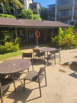 An outdoor seating area with round tables and wicker chairs, a Pepsi vending machine, and a lifebuoy on the wall. - Gorgeous Remodeled hotel suite in Princeville w/ pools & beach access, sleeps 4 (Princeville)
