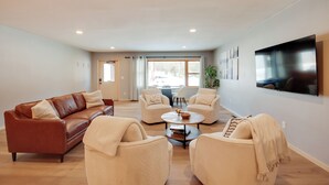 A modern living room with a brown leather sofa, two beige armchairs, a coffee table, and a flat-screen TV mounted on the wall. - Snowmobile & Enjoy Eagle River! ‘Southside Lodge’ (Eagle River)