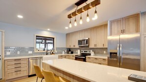 A modern kitchen with a large island, stainless steel appliances, wooden cabinets, and a window overlooking the city. - Snowmobile & Enjoy Eagle River! ‘Southside Lodge’ (Eagle River)