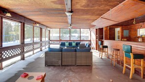 A covered outdoor seating area with wicker furniture, a wooden bar, and a view of the snowy landscape. - Snowmobile & Enjoy Eagle River! ‘Southside Lodge’ (Eagle River)