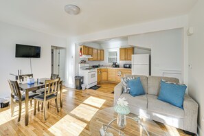 A modern living room with a wooden dining table, a sofa, and a TV mounted on the wall. - Cozy Cambridge Apartment in College Town! (Cambridge)