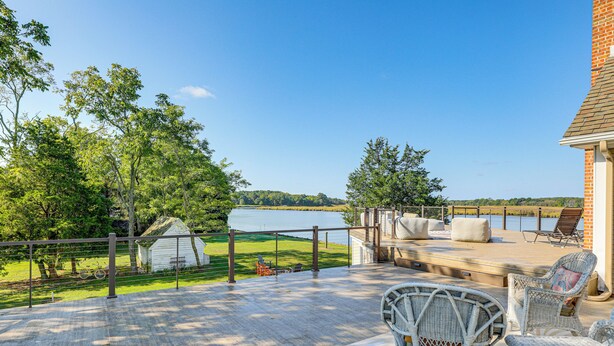A deck with wicker furniture overlooking a lake, a small shed, and a grassy area with a bicycle. - Riverfront Gem w/ Fire Pit in Eden (Eden)