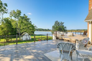 A deck with wicker furniture overlooking a lake, a small shed, and a grassy area with a bicycle.