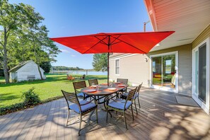 A deck with a table and chairs, a red umbrella, and a view of a lake and trees. - Riverfront Gem w/ Fire Pit in Eden (Eden)