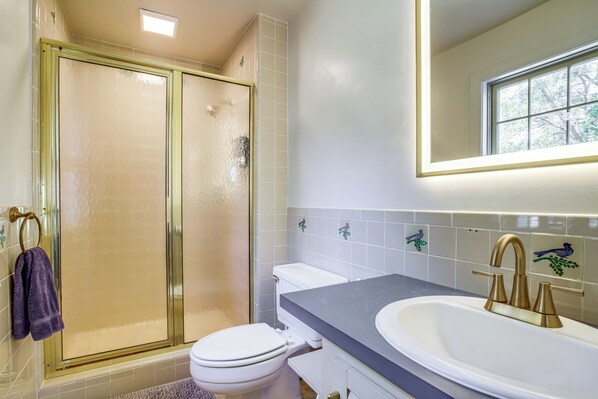 A bathroom with a glass-enclosed shower, a white toilet, and a sink with a gold faucet.