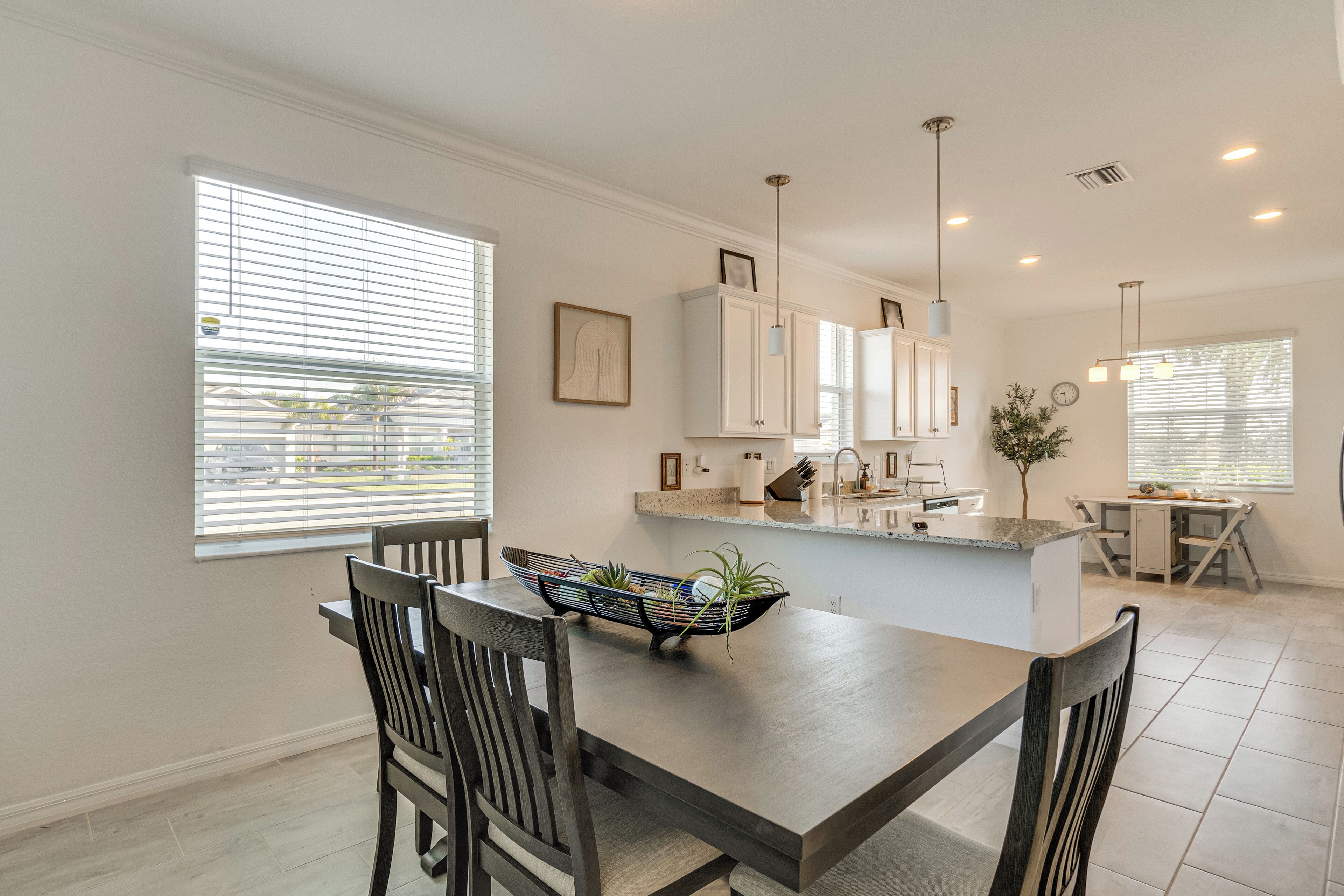 A modern kitchen with white cabinets, a dining table with chairs, and pendant lights.