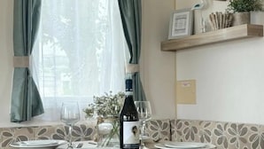Un comedor con una mesa dispuesta para dos personas, una botella de vino y un ventanal con cortinas.