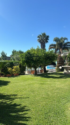 A well-maintained grassy area with trees, a pool, and a statue.