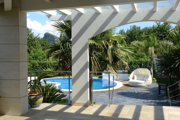 A covered outdoor area with a pool, lounge chairs, and potted plants.