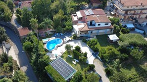 A residential area with a swimming pool, solar panels, and a two-story house with a tiled roof.