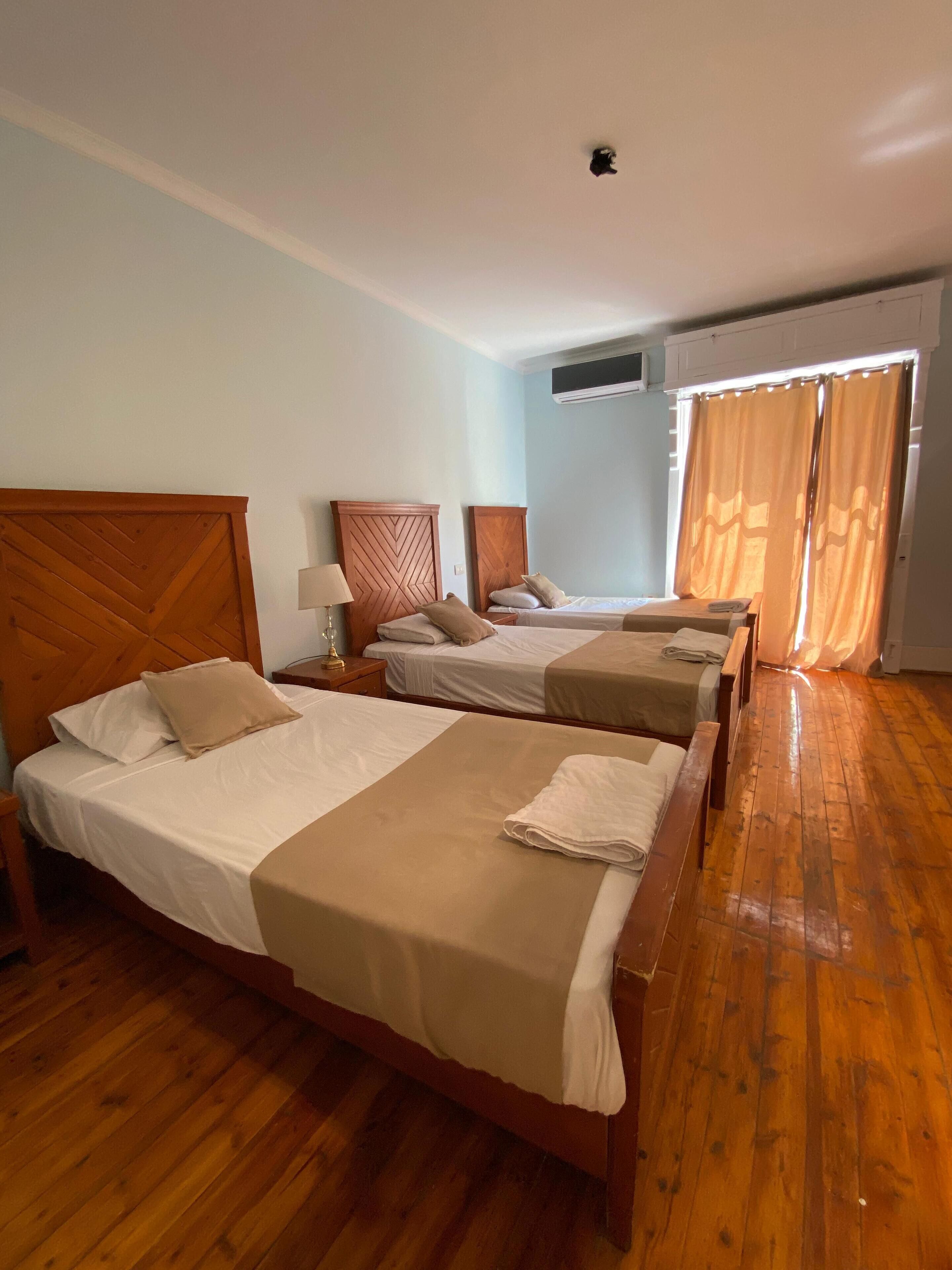 Habitación de hotel con tres camas de madera, suelo de madera y un equipo de aire acondicionado en la pared.