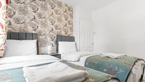 A hotel room with two beds, a nightstand, a white door, and a floral wallpaper.