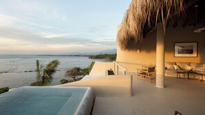 Un espace aménagé au bord de la piscine, avec vue sur l’océan, un toit de chaume et un coin salon comprenant un canapé et des fauteuils.