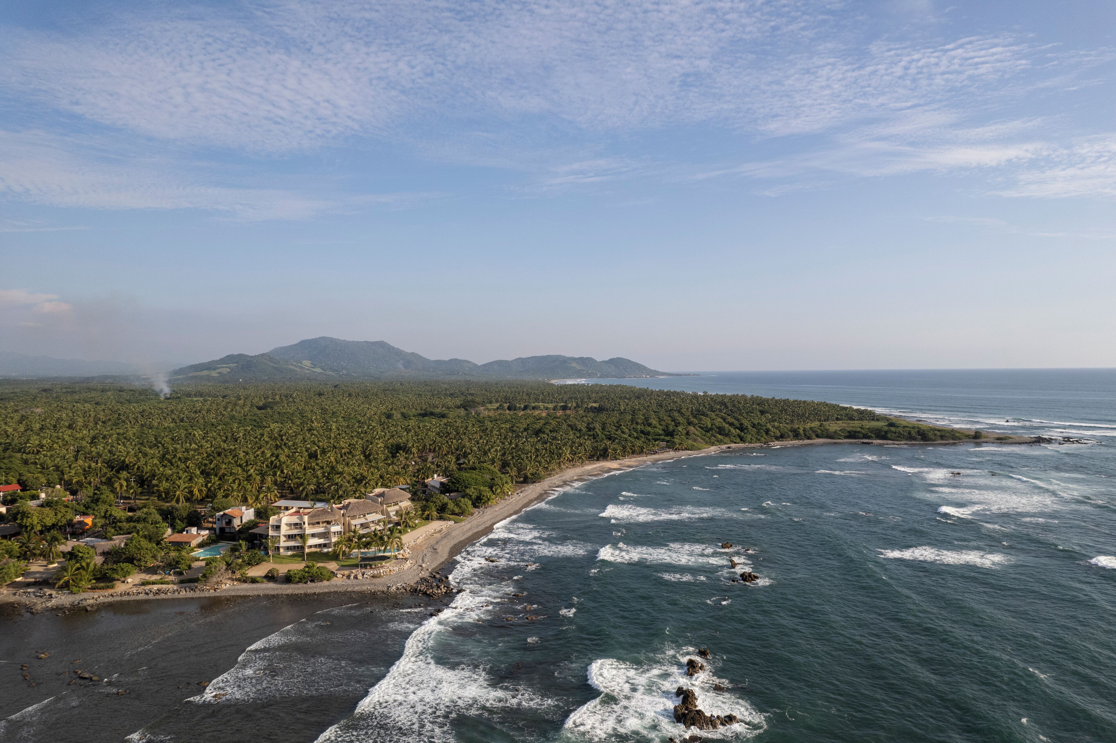 A coastal resort with beachfront properties, a sandy beach, and a forested area in the background.
