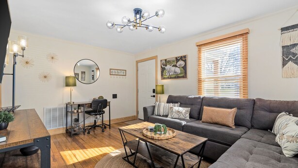 A modern living room with a gray sofa, a wooden dining table, and a ceiling light fixture.