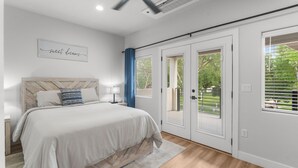 Ein Schlafzimmer mit Bett, Deckenventilator, Fenster mit Jalousien und einer Tür zu einem Außenbereich.