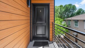 Ein modernes Gebäude mit einer schwarzen Tür, die mit der Nummer 4 gekennzeichnet ist, einer Holzfassade und einem Metallgeländer.