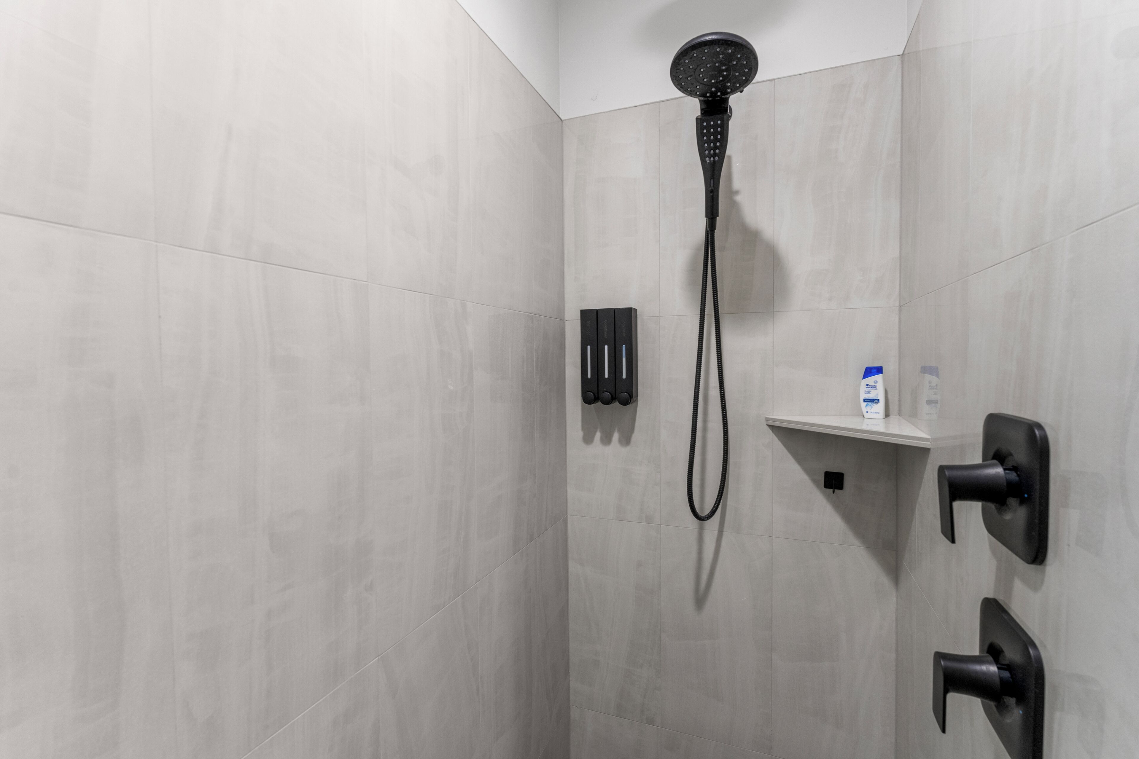 Une douche moderne équipée d’un pommeau de douche à main, d’un panneau de commande et d’une petite étagère pour les articles de toilette.