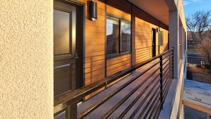 Ein Gebäude mit Holzfassade, einem Balkon mit Metallgeländer und blauem Himmel im Hintergrund.