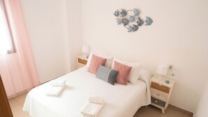Una cama bien hecha con almohadas y una toalla doblada, una mesita de noche con una lámpara y un adorno en la pared.