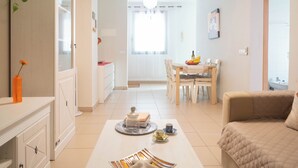 Una sala de estar moderna con un sofá color beige, un comedor con mesa y sillas de madera, y una cocina con armarios y encimera.