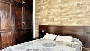 A bedroom with a wooden headboard, a large bed with patterned bedding, and a wardrobe with dark wood doors. - Pambnb - House next to the Beach, Terrace, Fiber Wi-Fi, BBQ (Abades)