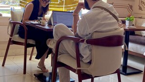 A hotel lobby with a large window displaying the hotel name, a fountain, and a cityscape view. There are two people seated at a table with a laptop. - lotus Altahrir hotel (Cairo)