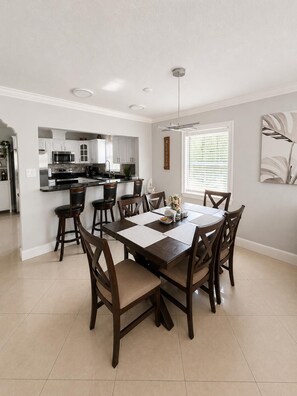 A modern kitchen with white cabinets, a central island, and a dining area with a large table and chairs.