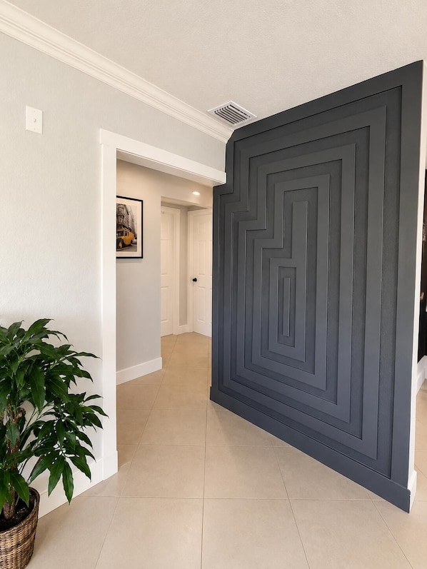 Un couloir avec une porte de couleur gris foncé, une plante en pot et un tableau encadré accroché au mur.