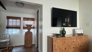 Una sala de estar con piso de madera, un sofá, un televisor montado en la pared y un perro acostado en el suelo.