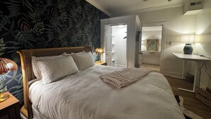 Un dormitorio con cama, ventilador de techo, mesita de noche con lámpara, cómoda y espejo.