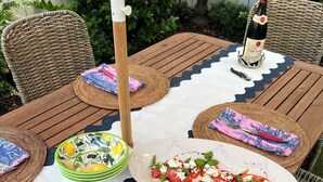 Una mesa de madera dispuesta para comer, con posavasos de mimbre, platos y una botella de vino.
