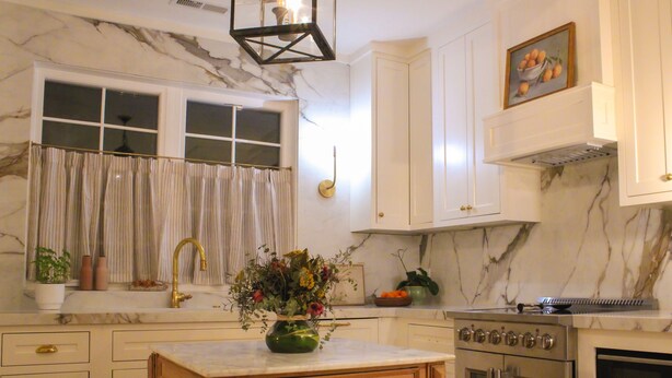 Una cocina con gabinetes blancos, salpicadero de mármol, una mesa de madera y electrodomésticos de acero inoxidable.