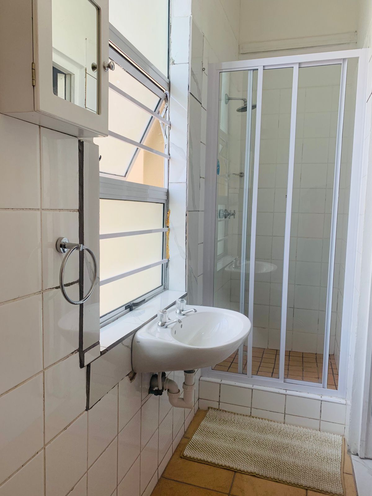 Un baño con lavamanos blanco, cabina de ducha de vidrio y suelo de baldosas.