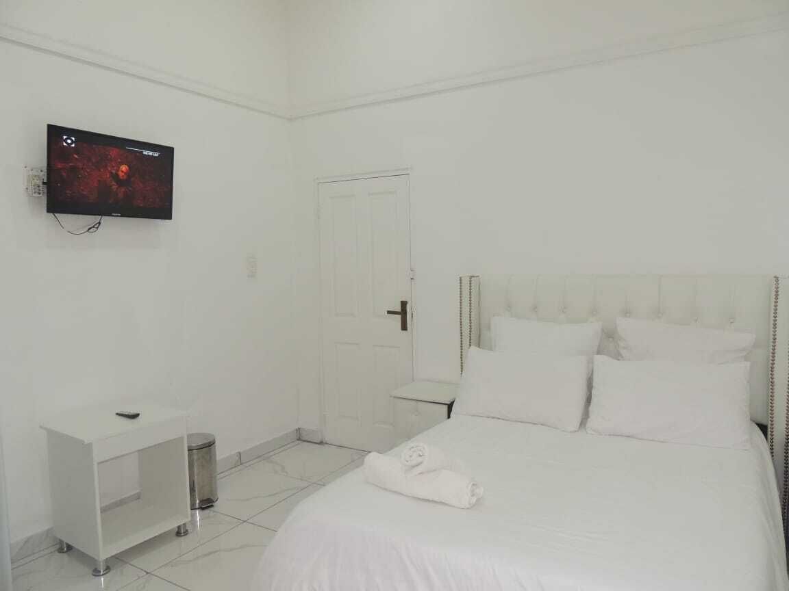 A hotel room with a bed, a TV mounted on the wall, a bedside table, and a door.