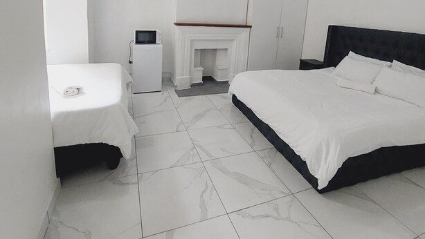Ein modernes Schlafzimmer mit einem großen Bett, einem kleineren Bett, einem Schreibtisch und einem Kamin.
