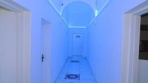 Ein schmaler Gang mit blau beleuchteter Decke und einer Tür am Ende.