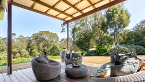 Un espacio de estar al aire libre techado con mobiliario de mimbre y vista a un paisaje natural.