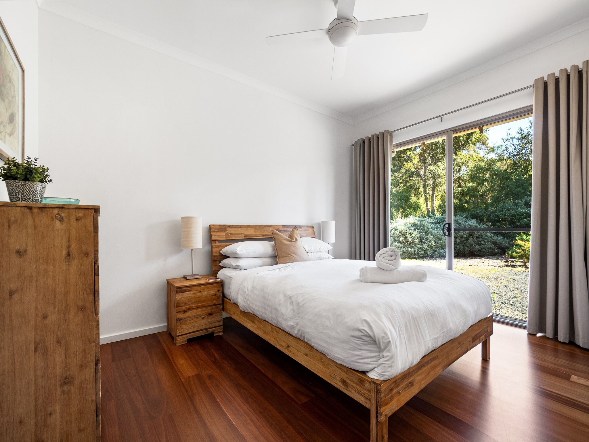 Una camera da letto con un letto di legno, un comodino, una ventola a soffitto e vista sul verde circostante.