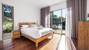 Un dormitorio con cama de madera, una mesita de noche, ventilador de techo y vistas al exterior a través de amplias puertas correderas de cristal.