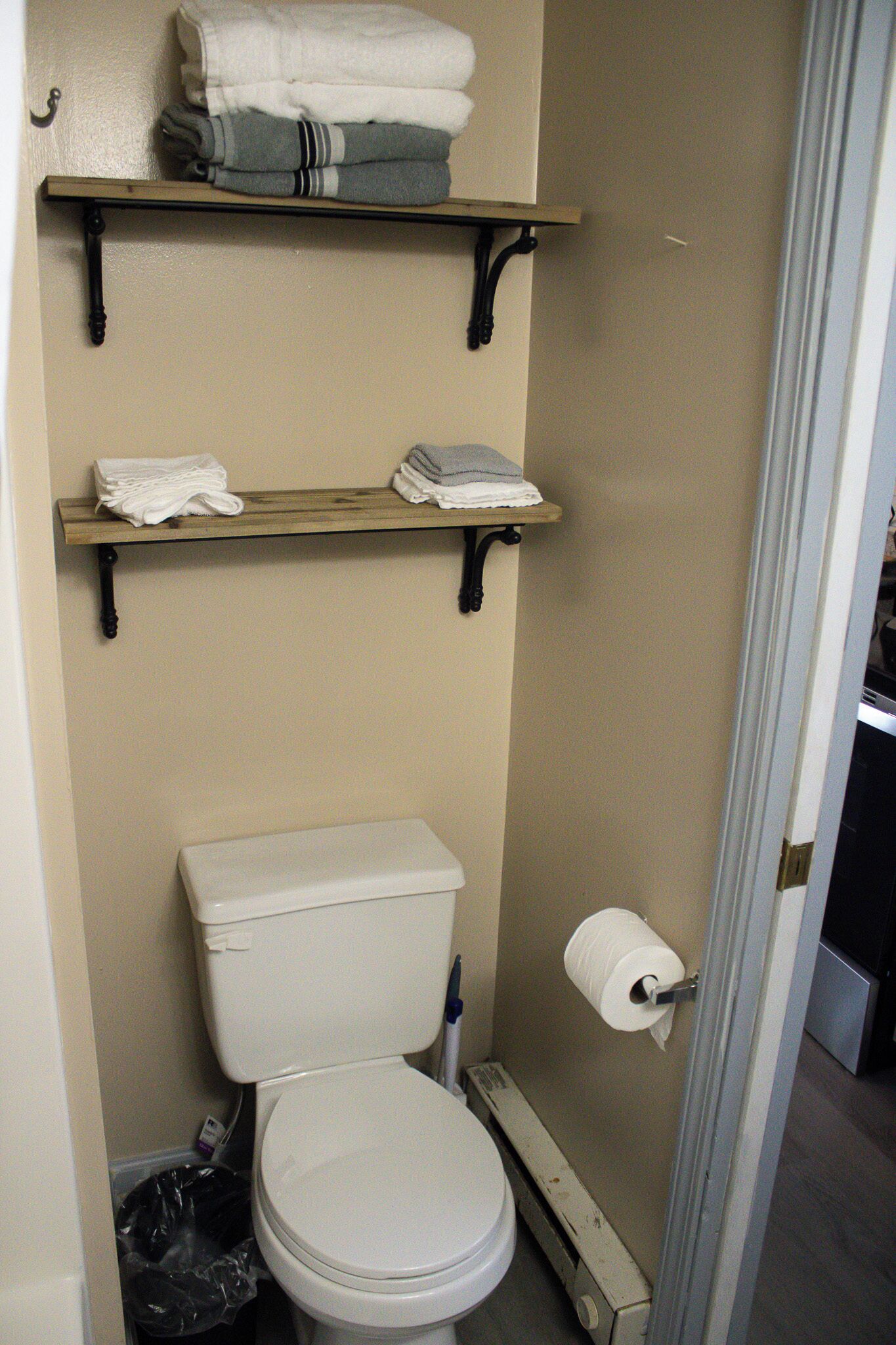 Ein Badezimmer mit Toilette, zwei Ablagen darüber und einer Toilettenpapierrolle an der Wand.