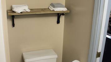 Ein Badezimmer mit Toilette, zwei Ablagen darüber und einer Toilettenpapierrolle an der Wand.