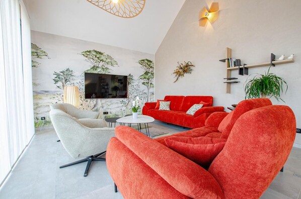 A modern living room with a large TV, red sofas, a white armchair, and a small round table.
