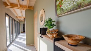 A hallway with a wooden ceiling, a large mirror, a wooden bowl, and a potted plant on a shelf.