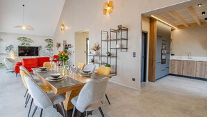 A modern dining area with a wooden table and grey chairs, a red sofa, and a kitchen with wooden cabinets and a built-in oven.
